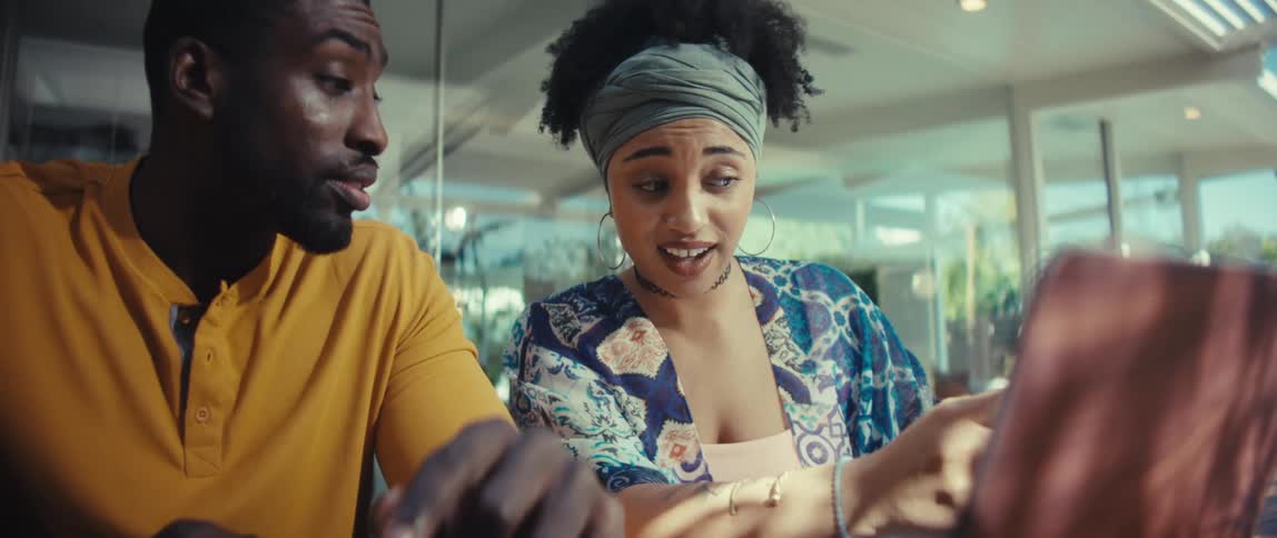 An enthusiastic young woman points at a laptop screen while collaborating with a male colleague in a bright, modern space