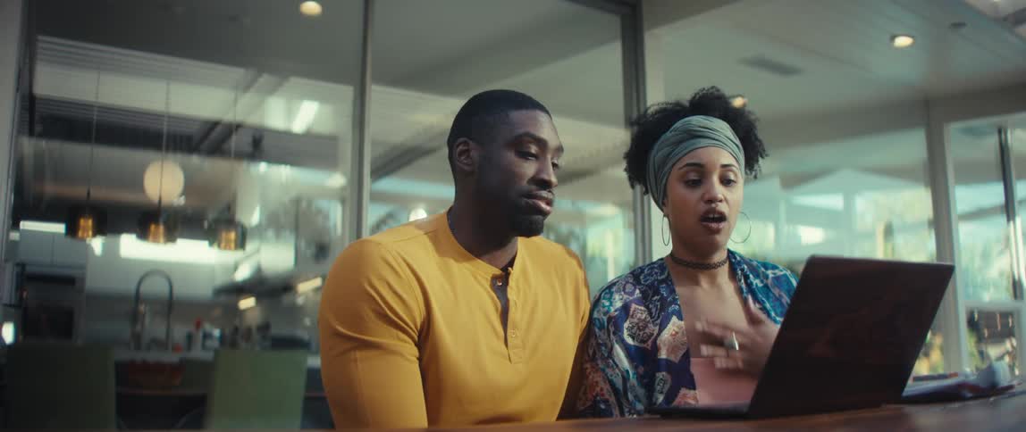A young African American couple's expressions change from happy to concerned and emotional while watching something together on a laptop