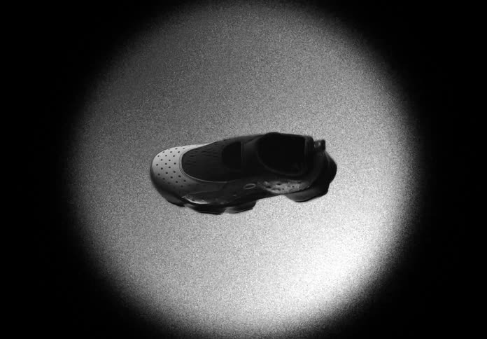 A futuristic black sneaker slowly rotates 360 degrees in a spotlight against a dark, grainy background