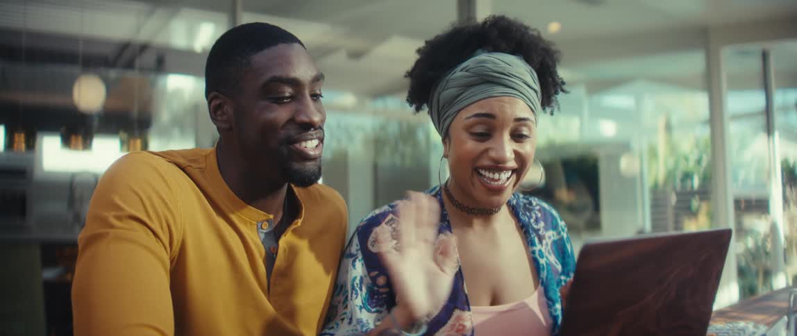 Happy young Black couple waves and smiles during a video call on their laptop in a stylish modern home