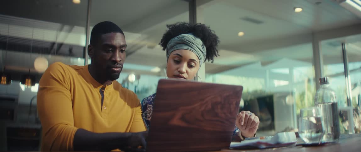 A focused young couple works collaboratively on a laptop in their modern, sunlit home office