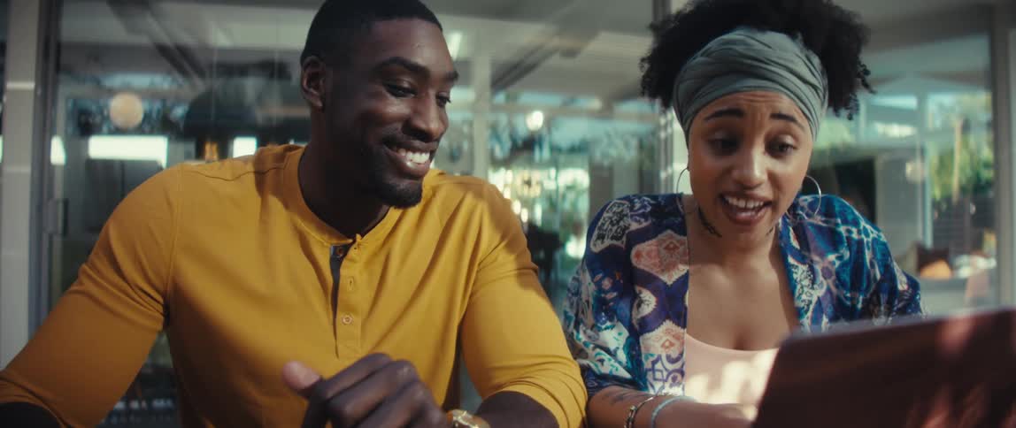 A cheerful young African American couple collaborates on a project, looking at a laptop with excitement in their modern sunlit home