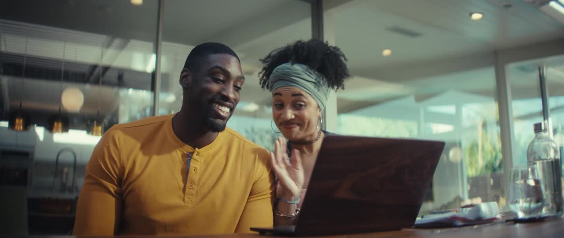 Slow motion shot of an excited couple talking and waving during a video call on a laptop in a bright, modern room