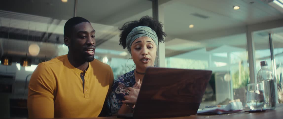 A young couple's joyful laughter turns to focused discussion as they collaborate on a laptop in a modern home