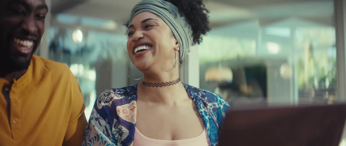 An ecstatic young couple erupts in joyful laughter while watching something on a laptop in slow motion
