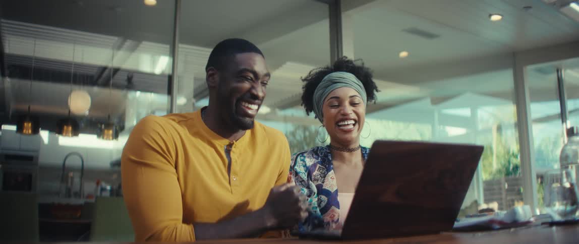 A joyful young Black couple shares a laugh while having a video call on a laptop in a bright, modern space