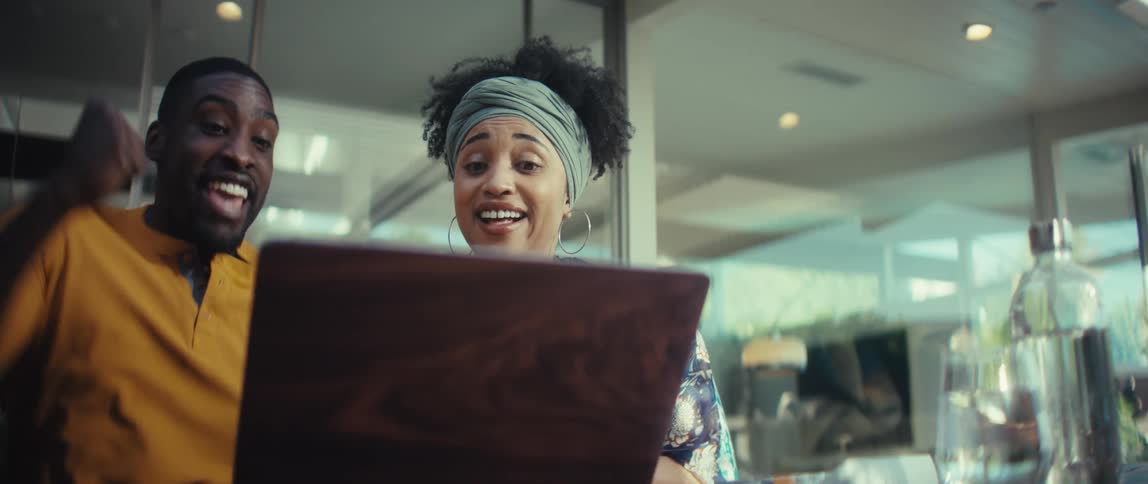 An ecstatic young couple erupts in cheers and celebration after receiving amazing news on their laptop in super slow motion