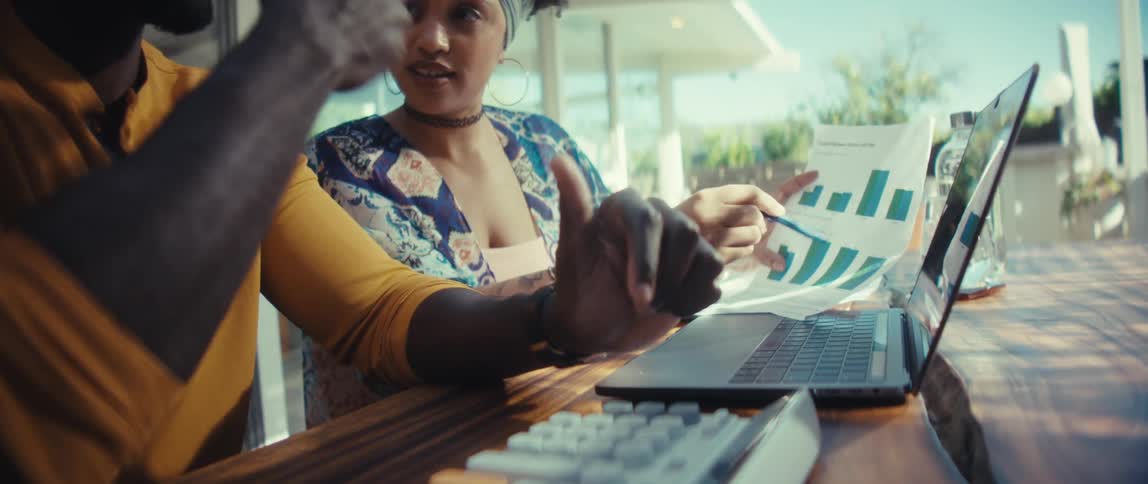 Close-up slow-motion shot of a young Black couple discussing finances, using a calculator, laptop, and business charts at a wooden table
