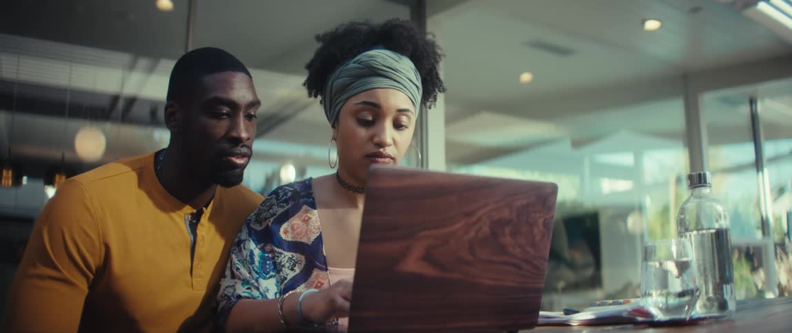 A stylish young Black couple opens a laptop to work together in a modern home, discussing their task before closing the computer