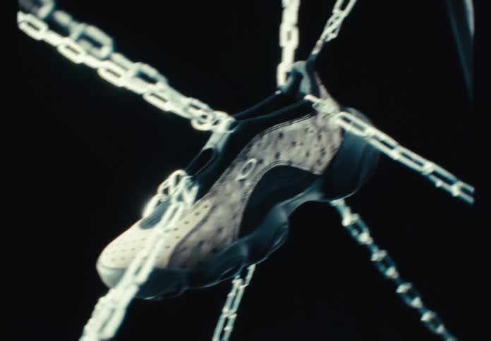 An artistic product shot of a modern sneaker suspended by heavy metal chains against a black background