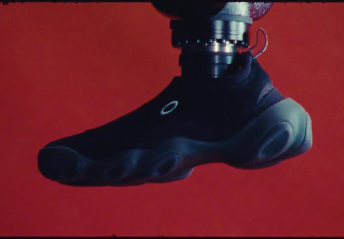 A robotic leg wearing a futuristic black sneaker is being tested in a lab with a vibrant red background