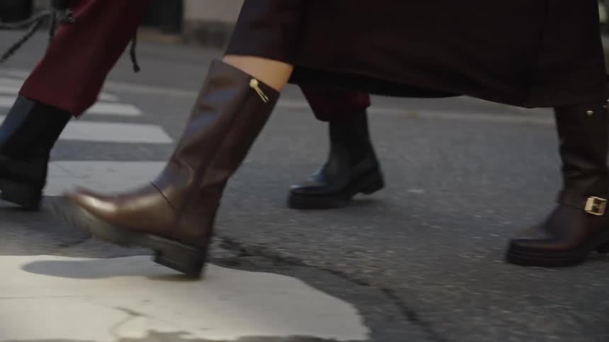 A close-up slow-motion shot of two women's stylish leather boots as they walk across a city street