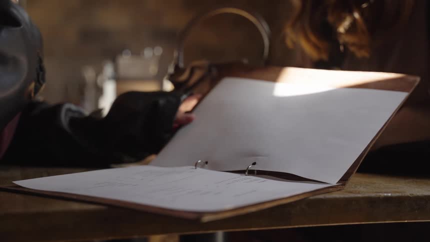 Slow motion close-up of a person browsing and then closing a leather-bound menu in a sunlit cafe