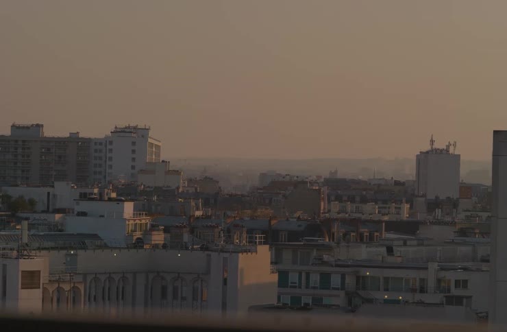 A slow panning shot reveals a hazy European cityscape bathed in the warm, golden light of an early morning sunrise