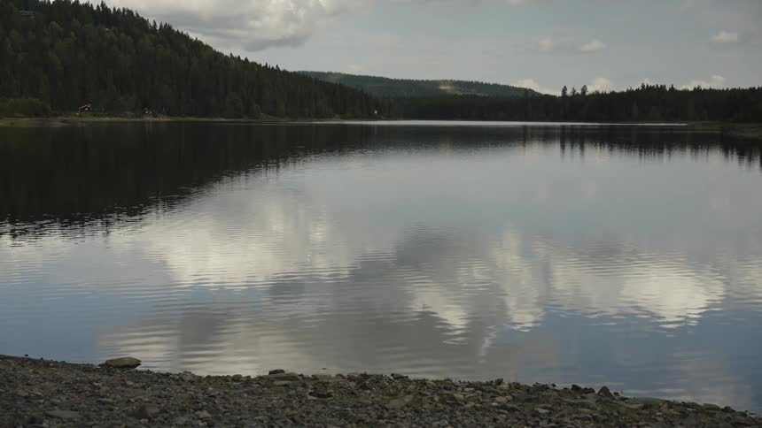 A tranquil mountain lake reflects the cloudy sky and surrounding evergreen forest