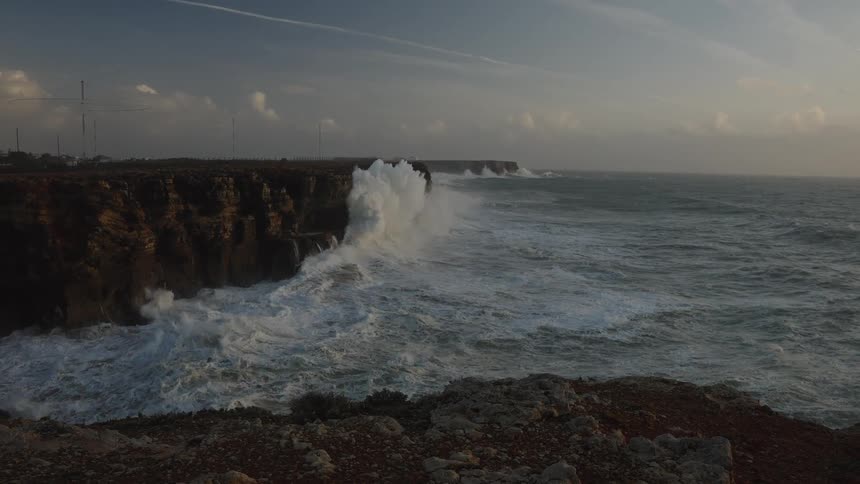 Dramatic slow-motion view of massive ocean waves crashing against the rugged cliffside of a coastline