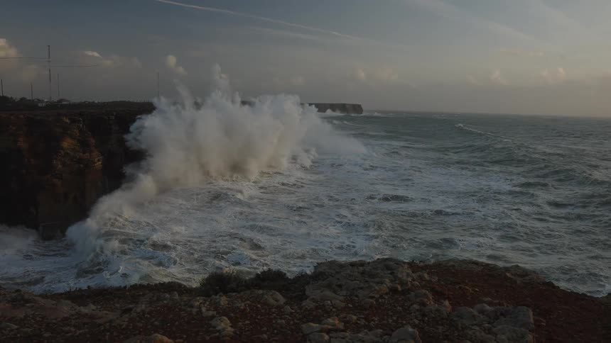 A powerful ocean storm sends massive waves crashing against a rugged cliffside in dramatic slow motion