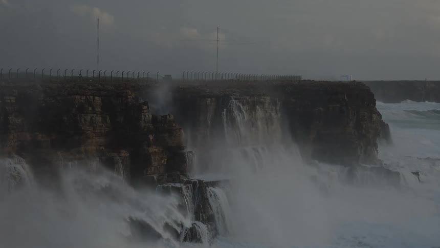 Massive white water waves from a powerful storm crash against a rugged coastline in dramatic slow motion