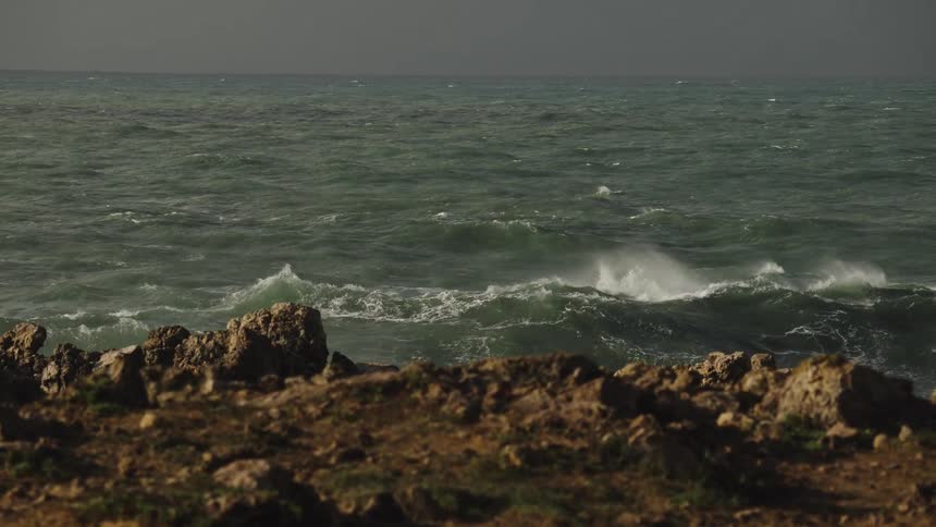 A powerful ocean wave crashes against a rocky shoreline in dramatic slow motion, sending a huge plume of sea spray into the air