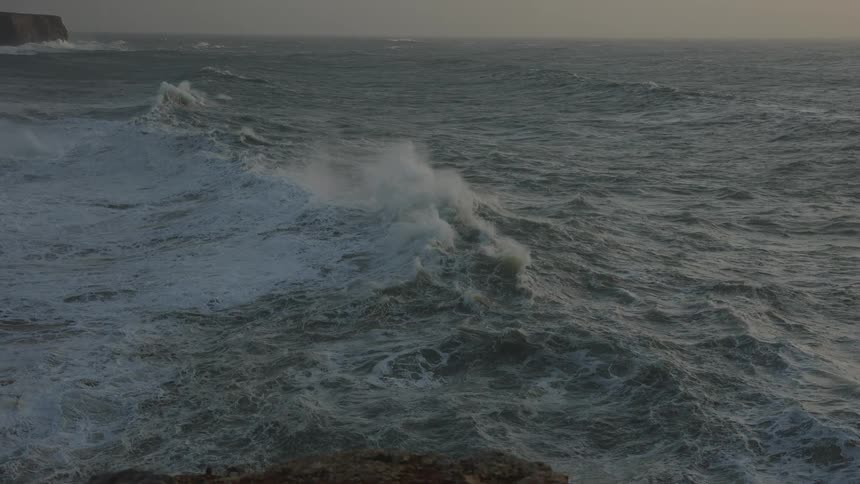A dramatic slow-motion shot of a turbulent ocean with massive waves crashing during a storm