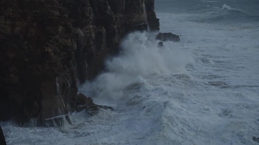Dramatic slow motion shot of massive storm waves crashing against a rugged sea cliff