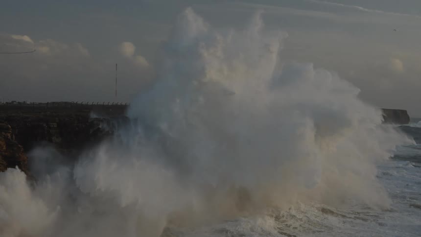 A powerful ocean wave crashes against a rugged cliffside in dramatic slow motion