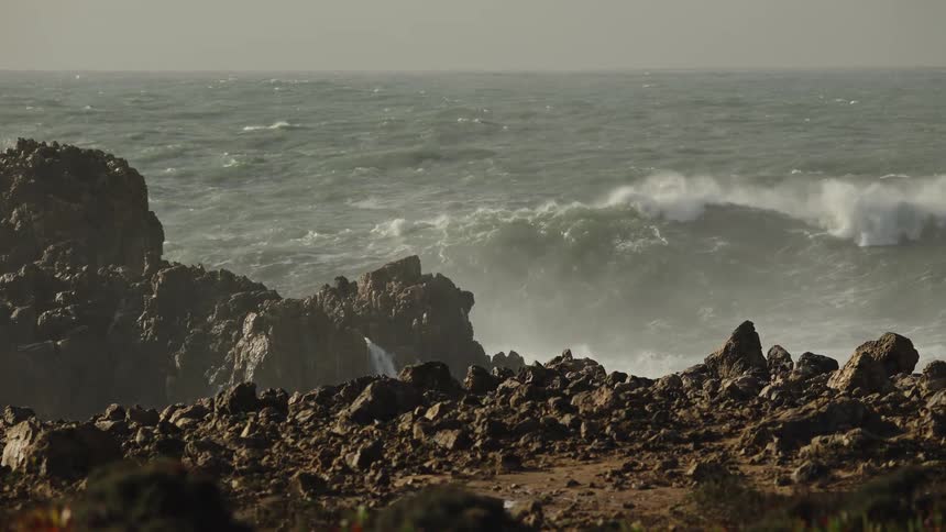 Dramatic slow motion captures the raw power of large ocean waves breaking on a rugged, rocky coast