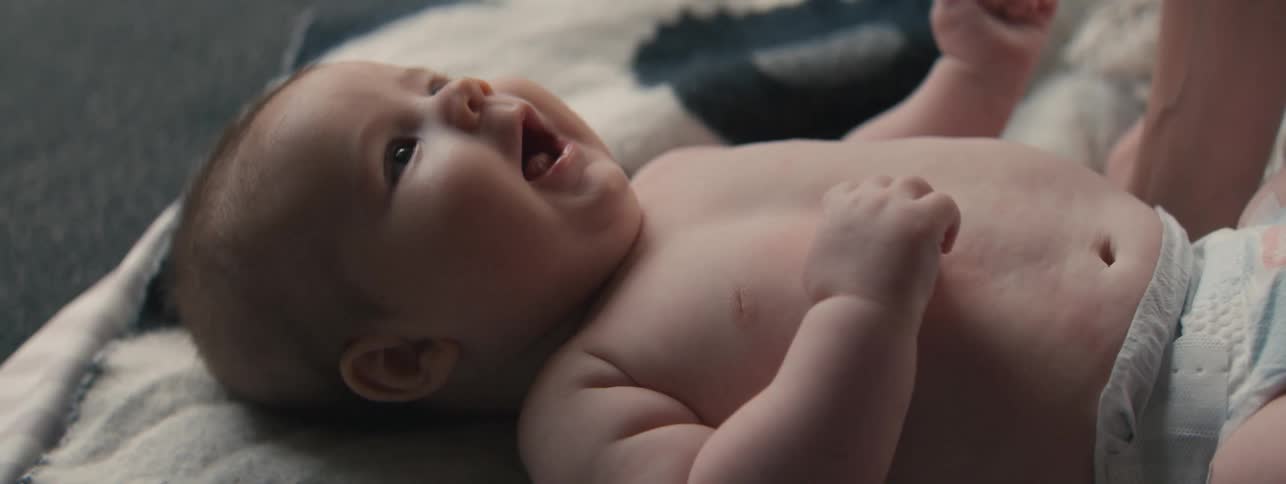 An adorable, happy baby lies on a blanket, giggling and cooing as their parent's hand gently tickles their chest and nose