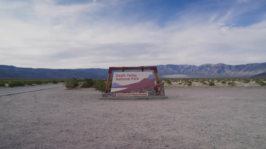 A quick zoom-out from the Death Valley National Park sign reveals the vast, arid desert landscape and distant mountains