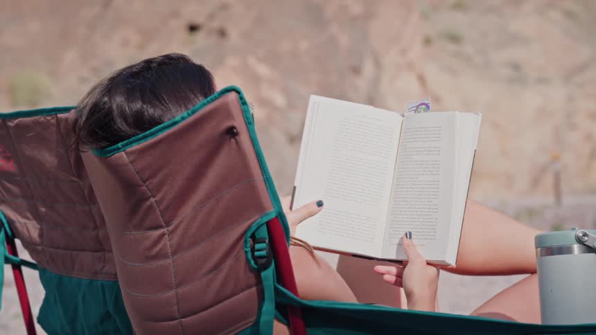 A woman relaxes in a camp chair while reading a book in a sunny desert setting