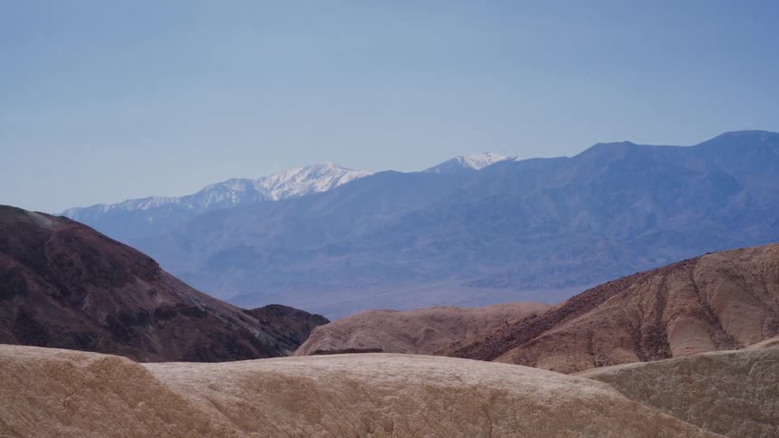 Zooming into the snow-capped Sierra Nevada mountains from the golden badlands of Zabriskie Point in Death Valley National Park