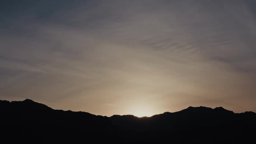A time-lapse of the sun rising from behind a silhouetted mountain range at dawn