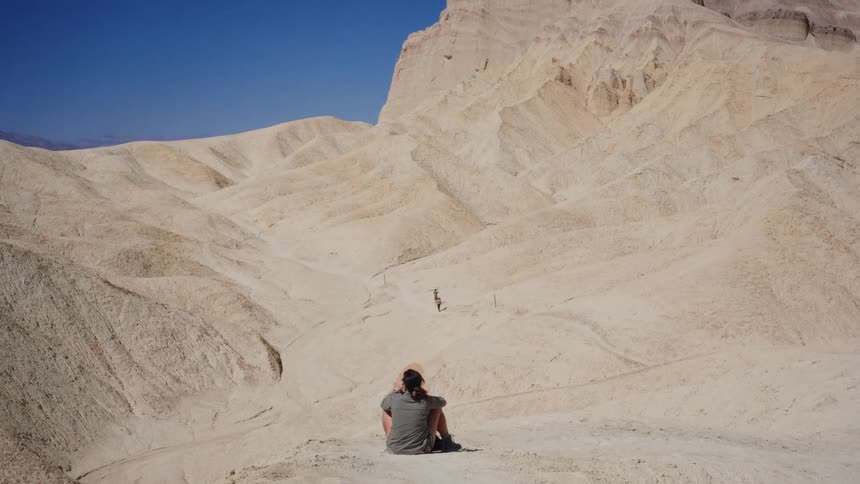 A lone traveler wearing a hat sits peacefully, gazing out at the expansive and sun-drenched badlands of a desert national park