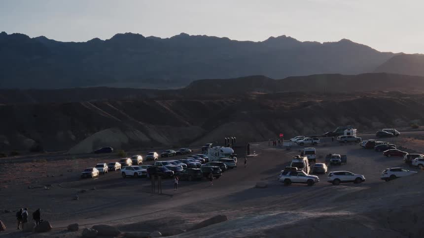 A helicopter lands in the crowded parking lot of a desert canyon viewpoint at sunset
