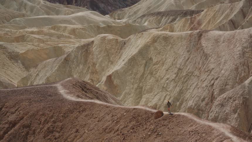 A lone hiker explores a winding trail through the vast, colorful and eroded badlands of Zabriskie Point