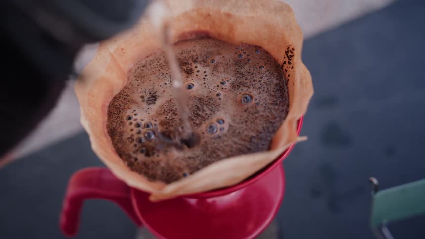 A captivating slow-motion close-up shows hot water being poured over fresh coffee grounds to brew a perfect cup of pour-over coffee