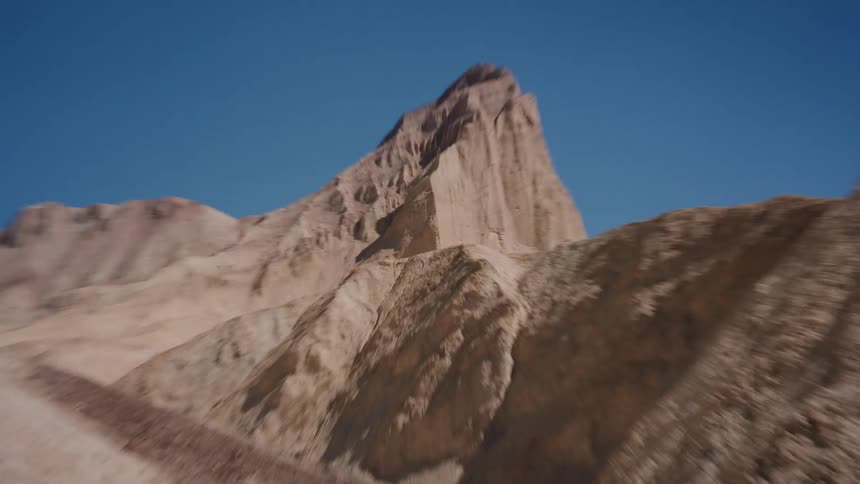 A slow zoom through a desolate, rocky desert canyon toward a jagged peak under a clear blue sky