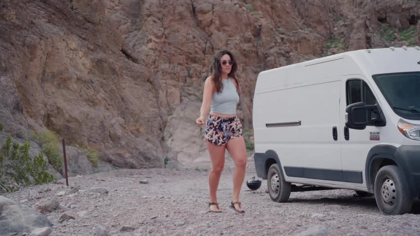 A free-spirited woman dances joyfully in slow motion at her desert campsite next to her camper van
