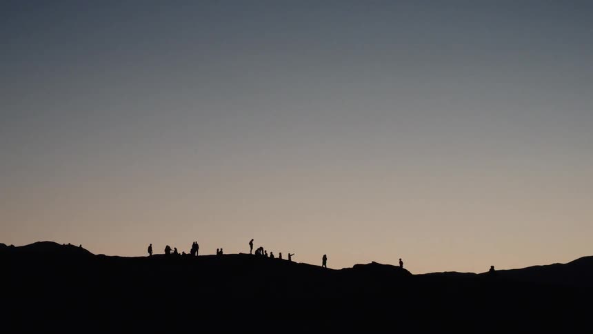 Silhouettes of a group of people stand on a mountain ridge against the vast, dusky sky