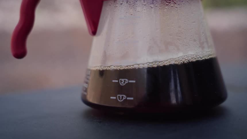 A close-up view of freshly brewed pour-over coffee in a glass carafe at an outdoor campsite