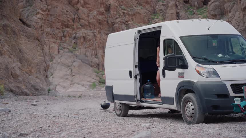 A man and woman get out of their camper van to start their day while camping in a remote rocky canyon