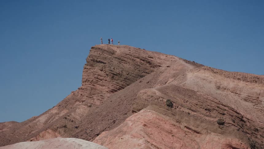 A small group of hikers stands on the summit of a majestic red rock mountain in the desert