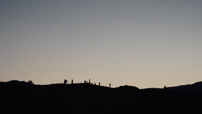 A long shot shows the silhouettes of a group of people standing on a hilltop against the fading light of dusk