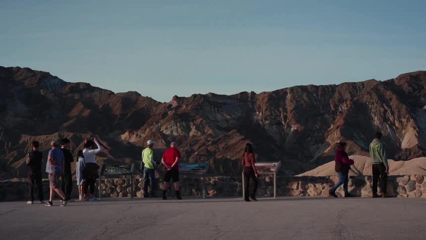 Tourists and sightseers gather at a scenic viewpoint to admire and photograph the vast, colorful badlands of a desert national park at sunset
