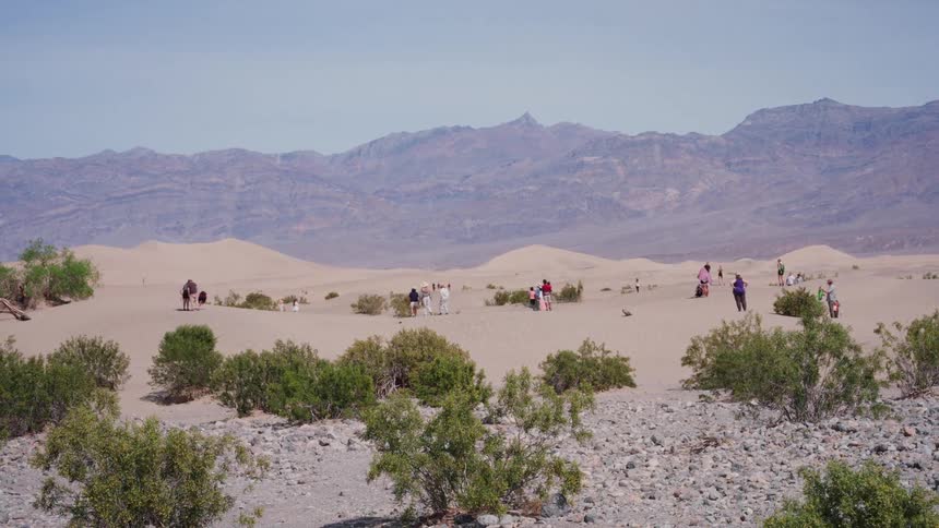 A wide view of tourists on the Death Valley sand dunes zooms in for a closer look at them exploring the arid landscape