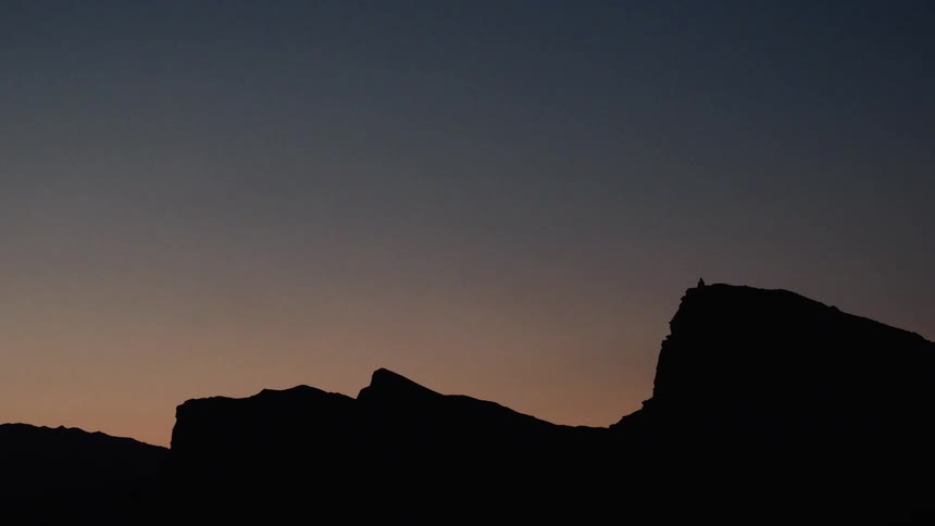 A serene silhouette shows a lone person sitting peacefully on a mountain peak against the beautiful gradient of a twilight sky