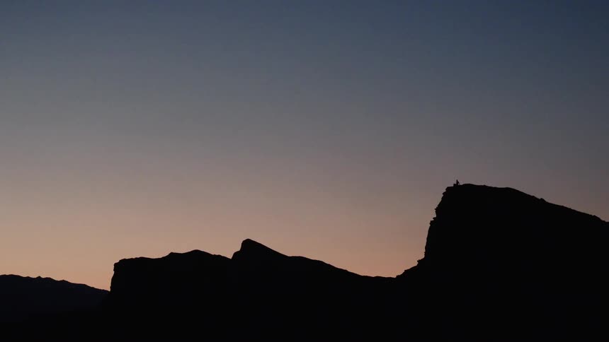 A lone person sits atop a mountain cliff, silhouetted against the serene twilight sky