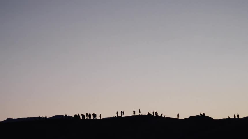 A large group of people are silhouetted on a distant hilltop against a clear dusk sky