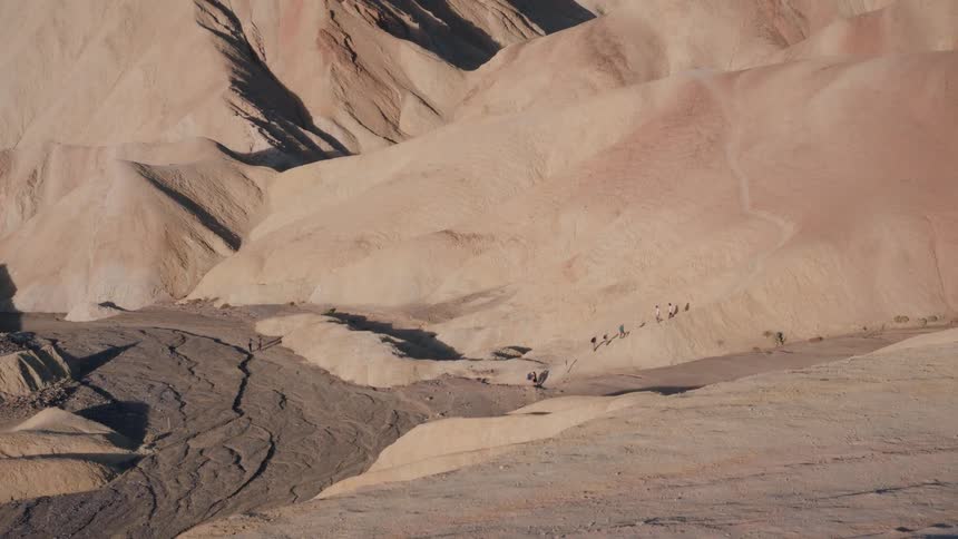 Hikers explore the vast and arid badlands of a desert canyon during golden hour