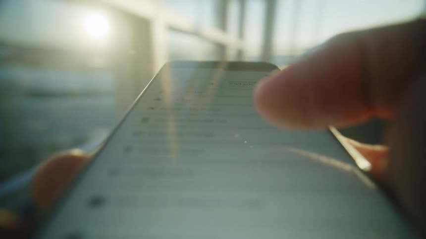 A traveler checks their digital boarding pass on a smartphone at a sunlit airport terminal before their flight
